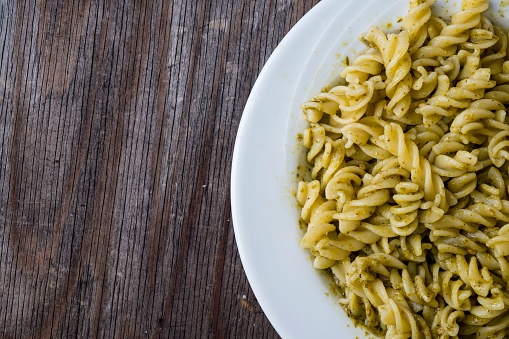 A plate of fusilli pasta with pesto sauce on a wooden table