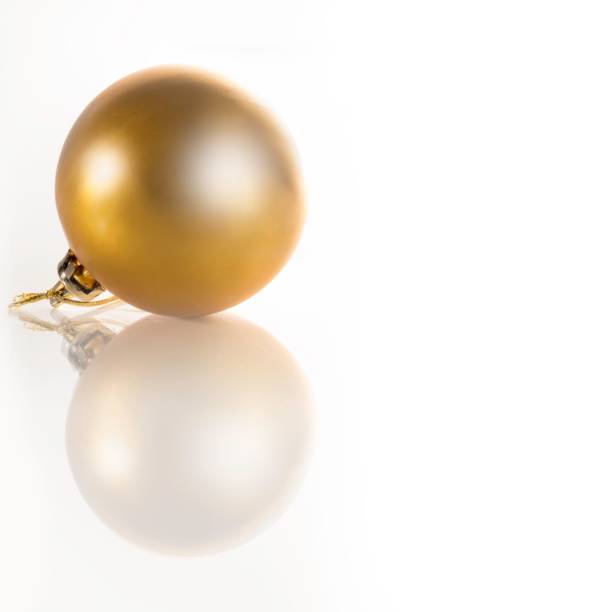 A closeup of a golden Christmas bauble reflected on a white surface