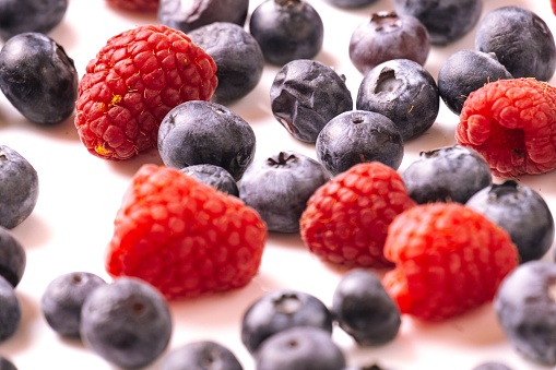 A closeup shot of fresh raspberries and blueberries on a white background