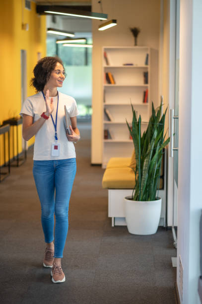 istock Cute office worker waving to her colleagues while passing by their room 1428380001