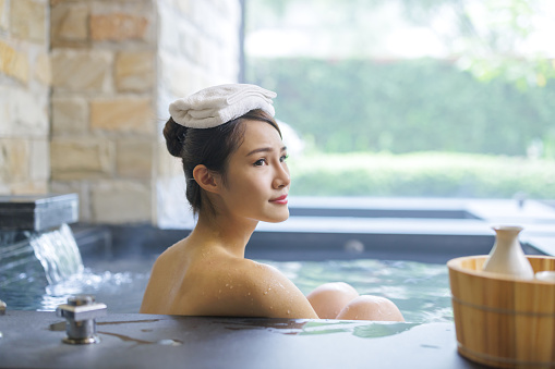 asian young woman and sake while she relaxing sitting in hot spring with towel on head