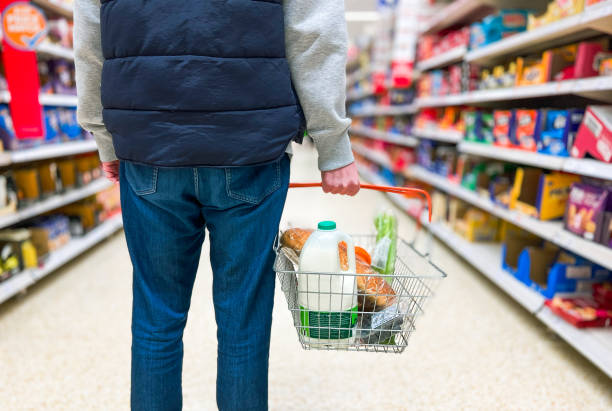 Man holding shopping basket with bread and milk groceries in supermarket Low angle close up color image depicting a man holding a shopping basked filled with essential fresh groceries like bread and milk in the supermarket. inflation stock pictures, royalty-free photos & images