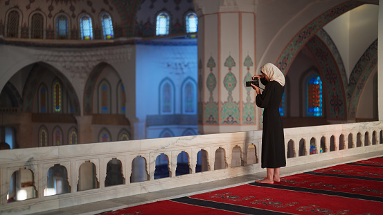 A foung female tourist is taking photos and videos in a mosque with her camera.