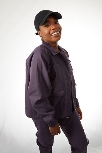 Lovely cheerful young black woman wearing a light gray jacket and a baseball cap