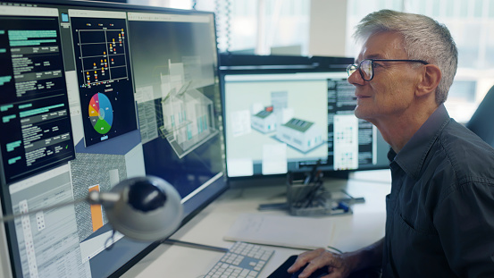 Stock image of a mature man working on a CAD design of an Eco house with\n associated data on screen.