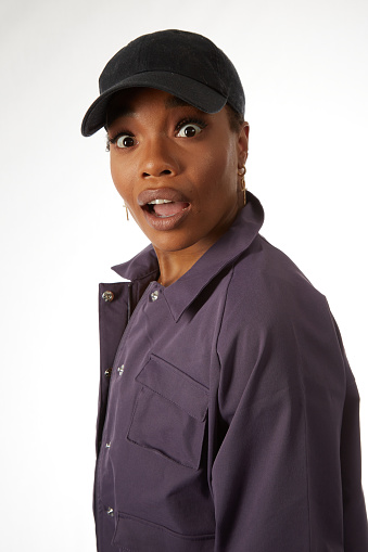 Lovely but astonished young black woman with bright eyes wearing a sports jacket and a baseball cap
