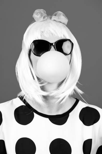 istock Woman with sunglasses blowing chewing gum bubble studio portrait 1428398538