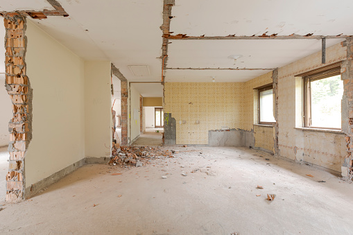 Large bright room with many windows of an old villa undergoing demolition and renovation. The walls have been knocked down and the floor is gone. Nobody inside