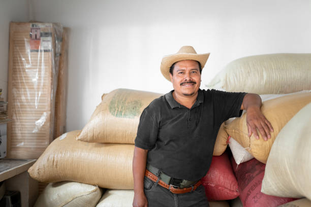 porträt eines hispanischen bauern, der neben seinen kaffeesäcken im lagerhaus lächelt - coffee sack bag warehouse stock-fotos und bilder