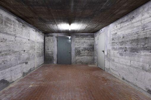 Front view of reinforced concrete wall of a bunker with closed armored door. Scene illuminated by a white neon lamp. Nobody inside