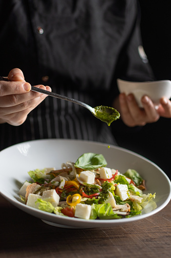 Female chef pouring sauce from the spoon on the salad dish on a black background.