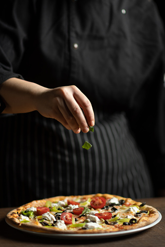 Female chef in restaurant decorates a pizza margherita.