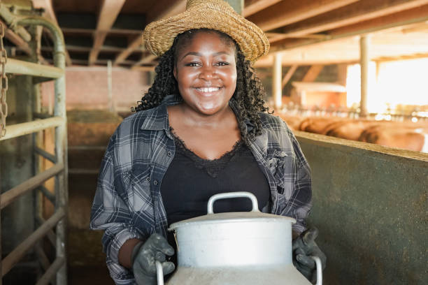 feliz mulher agricultor africano sorrindo na câmera dentro de galpão enquanto segurava lata de leite - farmer color image photography switzerland - fotografias e filmes do acervo