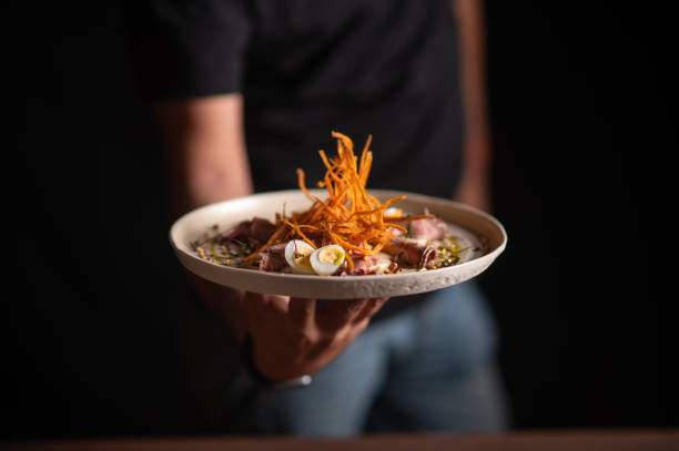 uno chef maschio che serve un piatto raffinato in un ristorante - servizio di lusso foto e immagini stock