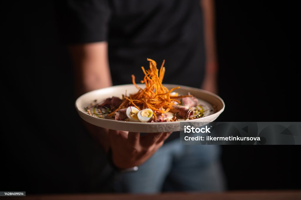 A male chef serving a fine dining dish in a restaurant A male chef serving a fine dining dish in a restaurant. Close-up Stock Photo
