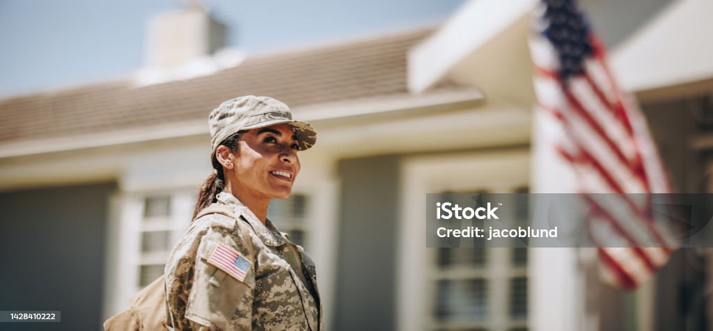 Happy female soldier returning home from the military Happy female soldier looking away with a smile while standing outside her house with her bag. American servicewoman coming back home after serving her country in the military. Veteran Stock Photo