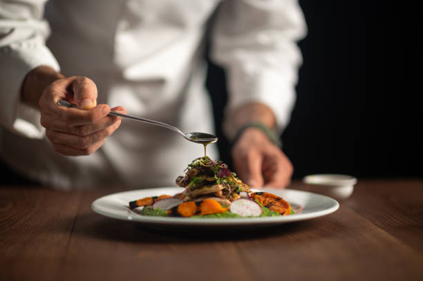 ein männlicher koch, der sauce auf die mahlzeit gießt - essen am tisch stock-fotos und bilder