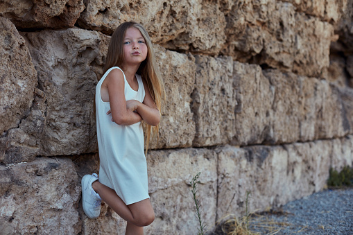 Little cute girl is posing against a historical stone wall in a historical area.