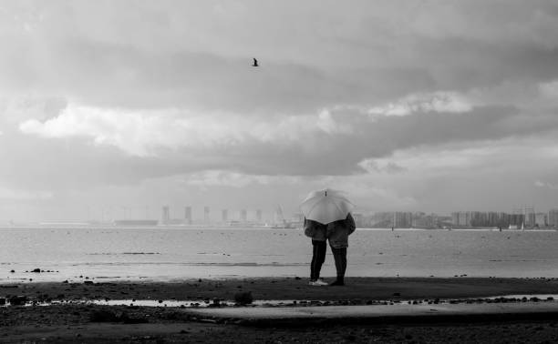 romantic young couple hiding behind the umbrella and standing in near sea or lake