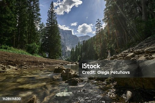 istock a rocky mountain and stream flows in a valley, a mountain stream running through a forest under a partly cloudy sky 1428414830