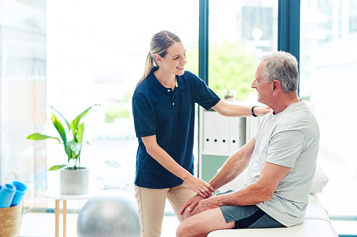 Senior man with nurse at chiropractor doing physiotherapy in consultation room. Old man with injury from sports or exercise with a doctor or physiotherapist health worker doing physio training