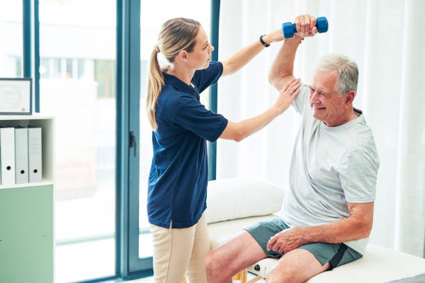 Physiotherapy, fitness and elderly man with nurse help training arm muscle for healthcare, workout and support. Exercise, consulting and medical caregiver stretching senior patient for rehabilitation stock photo