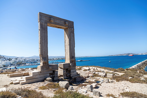 Naxos island, Temple of Apollo, Cyclades Greece. Portara, marble pillars gate on islet of Palatia, sunny day, calm sea, Naxos harbor, building, blue sky background.