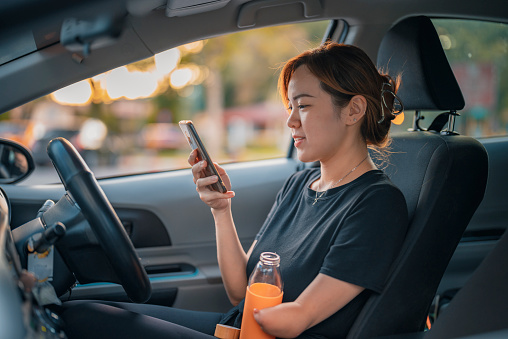 Chinese woman with disability deformed arm amputee texting message drinking water before starting her journey sitting on driver seat at parking lot