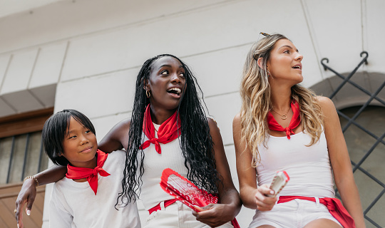 A boy and two girls of different ethnicity, sitting on a wooden barrier, watch the running of the bulls with surprise. Concept of fun, tolerance and diversity in popular festivities. san fermin