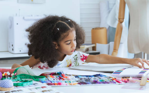 Cute African little girl drawing or sketching clothing design on paper at tailor room, cozy home as her career dream, smiling with happiness and fun. Leisure, Lifestyle, Education, Kid Concept. Cute African little girl drawing or sketching clothing design on paper at tailor room, cozy home as her career dream, smiling with happiness and fun. Leisure, Lifestyle, Education, Kid Concept children only stock pictures, royalty-free photos & images