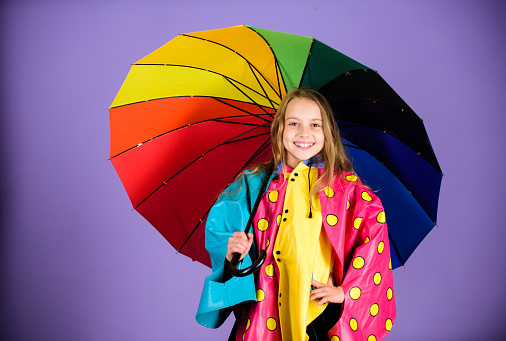 Kid girl happy hold colorful umbrella wear waterproof cloak. Enjoy rainy weather with proper garments. Waterproof accessories for children. Waterproof accessories make rainy day cheerful and pleasant.