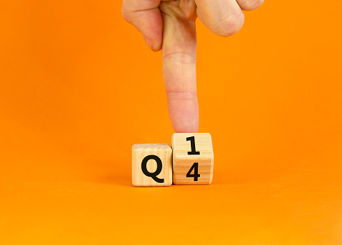 From 4th to 1st quarter symbol. Businessman turns a wooden cube and changes words 'Q4' to 'Q1'. Beautiful orange table, orange background. Business, happy 1st quarter Q1 concept, copy space.