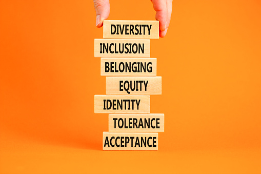 Diversity, inclusion symbol. Diversity belonging inclusion equity identity tolerance acceptance words on blocks. Businessman hand. Beautiful orange background. Diversity inclusion belonging concept.