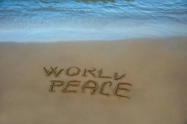World peace written in the sand on the beach with the sea washing up the shore.