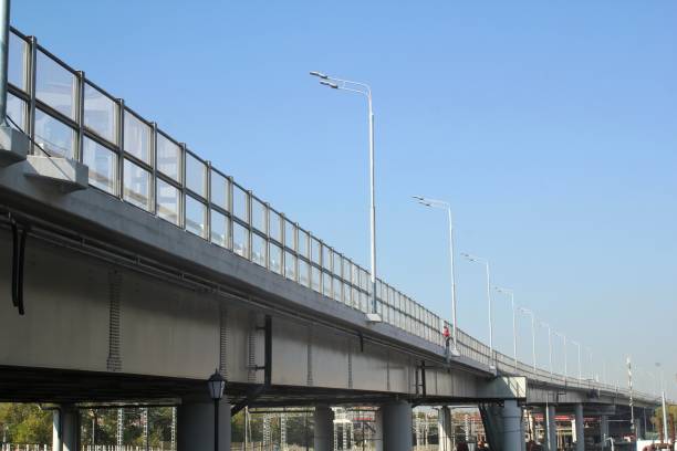 istock Low angle view of modern bridge highway long overpass with fencing and lighting system illumination on blue sky background 1428433146