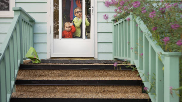 Cute little boys pressing their faces against their front door Two adorable little brothers pressing their faces against the window of their front door at home looking out front door stock pictures, royalty-free photos & images