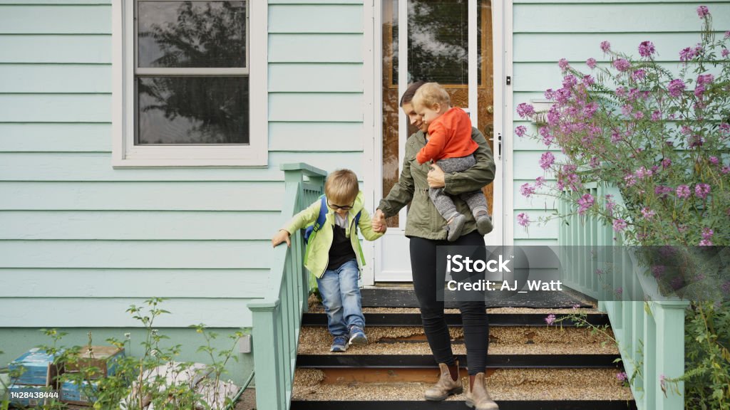 Mom and her little sons walking down the front steps of their home Mother and her two cute little sons walking down the front steps of their house Family Stock Photo