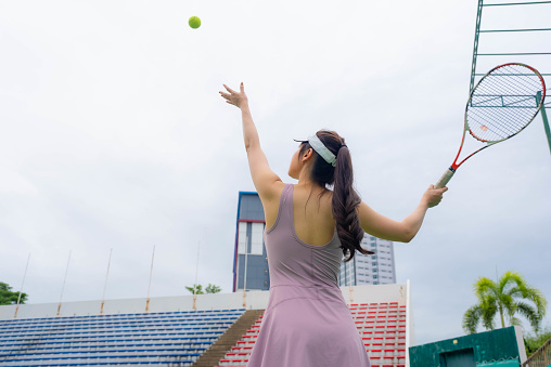 Young female tennis player practice  hitting tennis ball against at the outdoor tennis court.