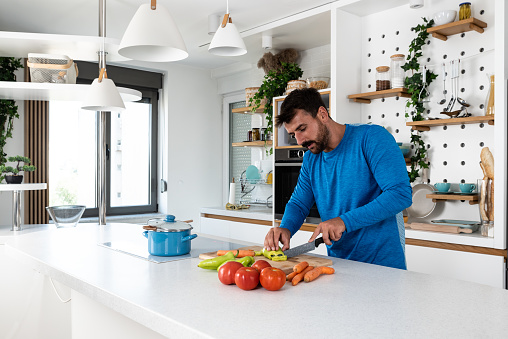 Young man cancer survivor cooking and preparing vegetarian meal after long heavy sickness. Vegan male in the kitchen making healthy lunch from fresh vegetables changing way of life after illness.