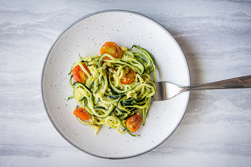 plate of zucchini spaghetti with cherry tomatoes on a light gray background