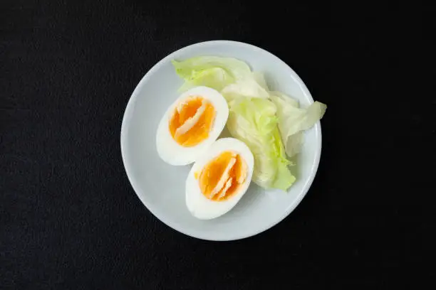 Halves of a hard-boiled chicken egg with lettuce greens on a plate on a dark background - top view