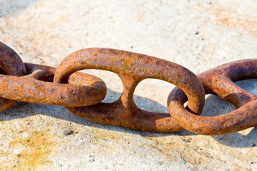 Detail of an old rusty metal chain anchored to a concrete block