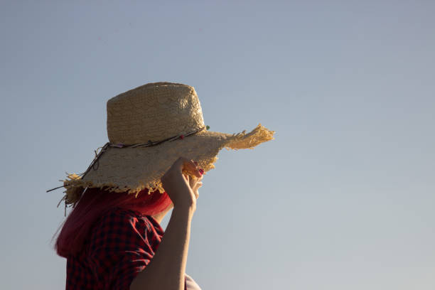 Unrecognizable woman wearing red dress picking accessories to her outfit holding big sun hat.