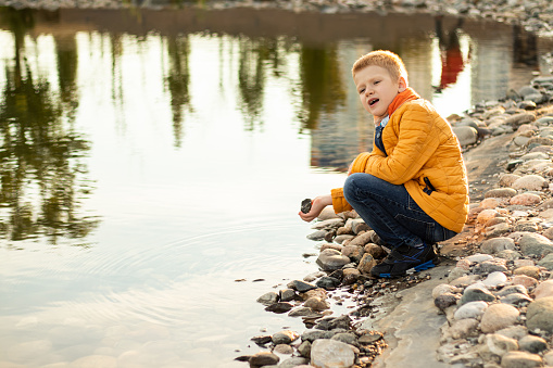 Child walking in the park sits down on stones near city pond to rest and meditate
