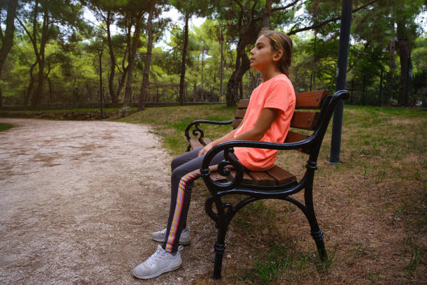 11 year old girl with braided hair. Sportswear. Woodland, nature. Pine trees, lawn. The girl is wearing an orange T-shirt.Side profile.