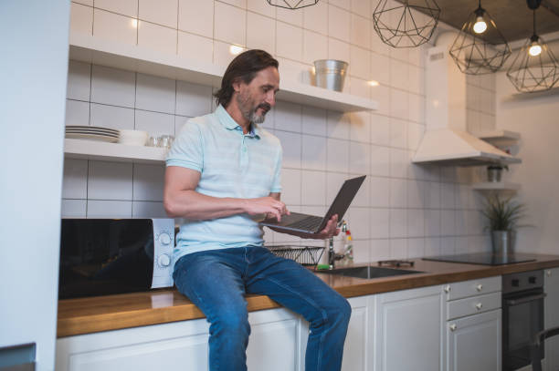 istock Man sitting on the table in the kitchen with a lapotp 1428462637