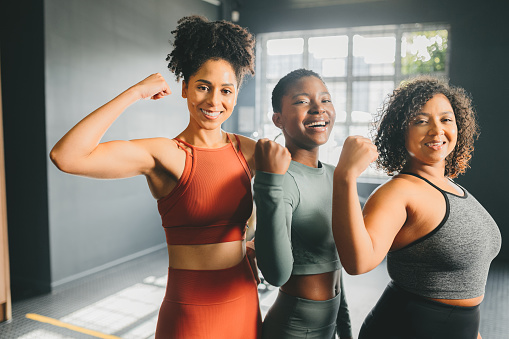 Fitness, training and working with strong women flexing their muscle or bicep in a gym or studio. Motivation, sport and workout with a female athlete and friends in a health center for wellness