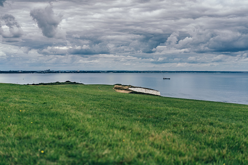 Seacoast, green grass, blue sea and moody sky with dramatic clouds.