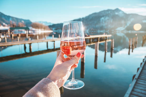 female hand with glass of rose wine. cozy pier on the coast of the lake tegernsee. alpine mountains in bavaria - lake tegernsee imagens e fotografias de stock