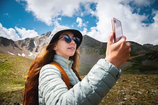 Young caucasian woman smiling and taking a selfie photo on a mountain plateau, hiking with backpacks, alpine view.